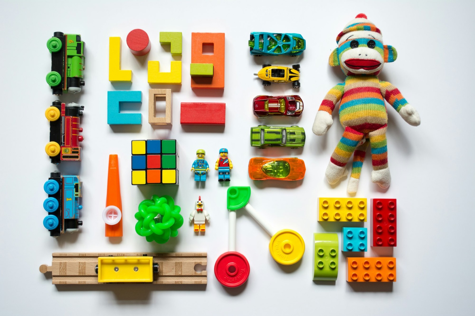 Colorful toy trains, blocks, cars and a plush sock monkey laid out flat on a white background