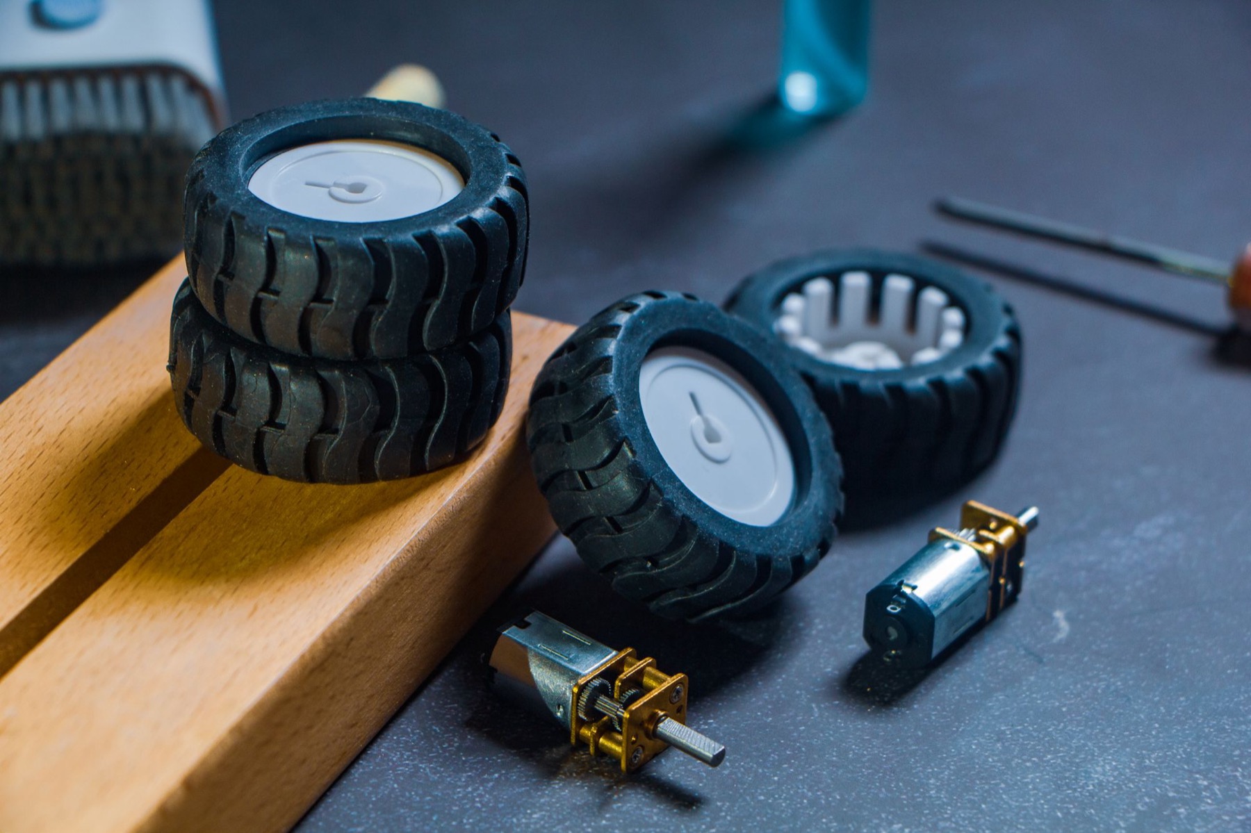 Black rubber robot wheels and small gear motors laid out on a dark workbench beside a wooden block