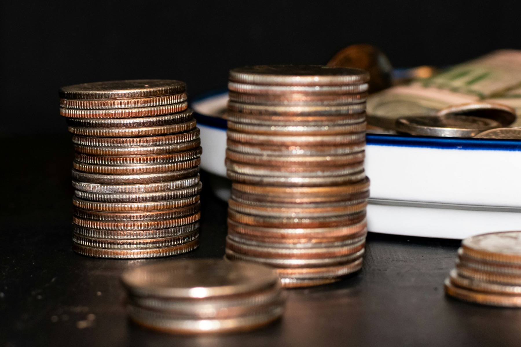 Two tall stacks of coins on a dark table, with a notebook and paper bills behind them